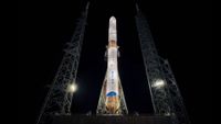 a white and blue rocket standing on its launch pad at night.