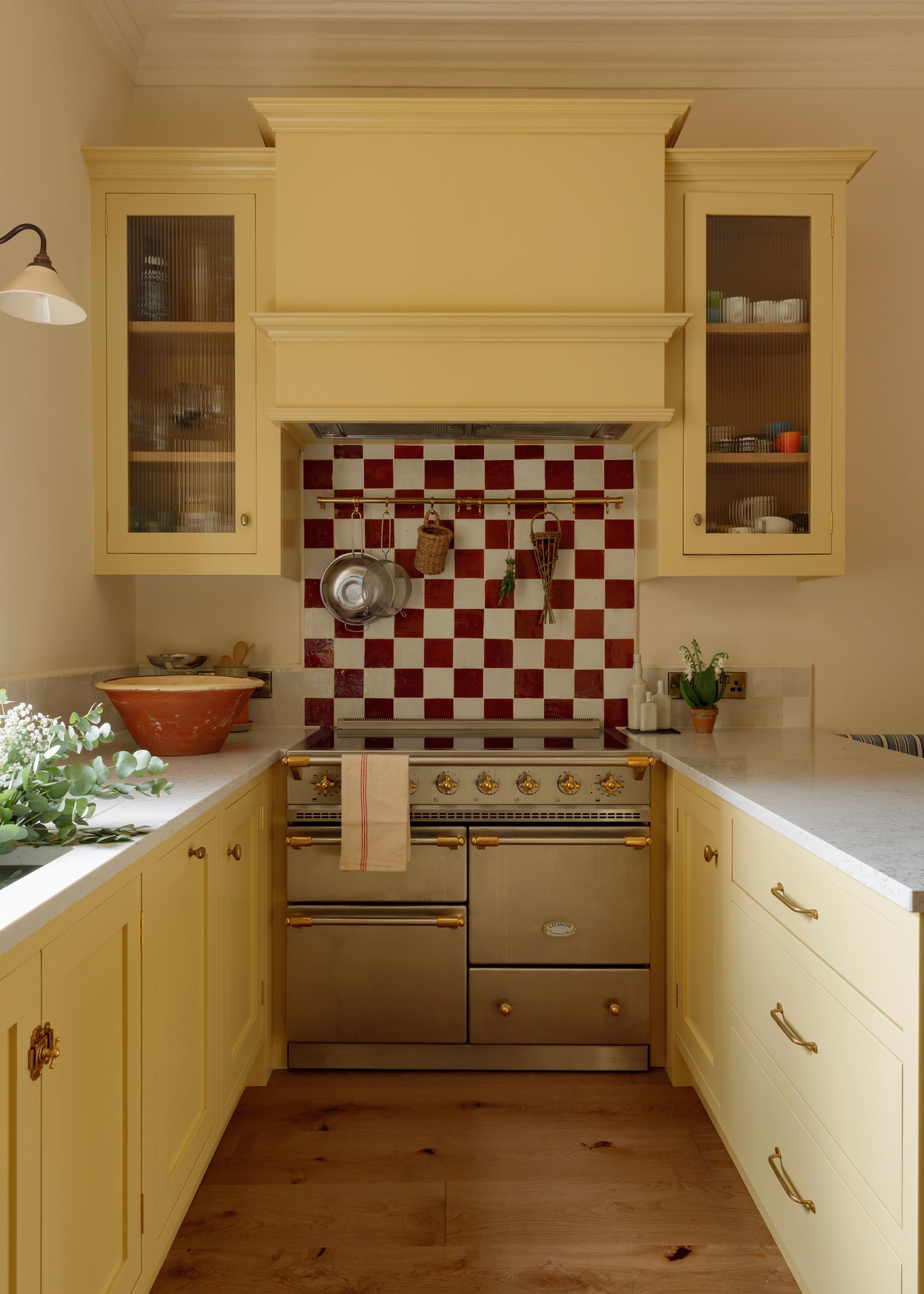 A narrow kitchen with yellow kitchen cabinets and a red and white checkered tile backsplash above the range cooker