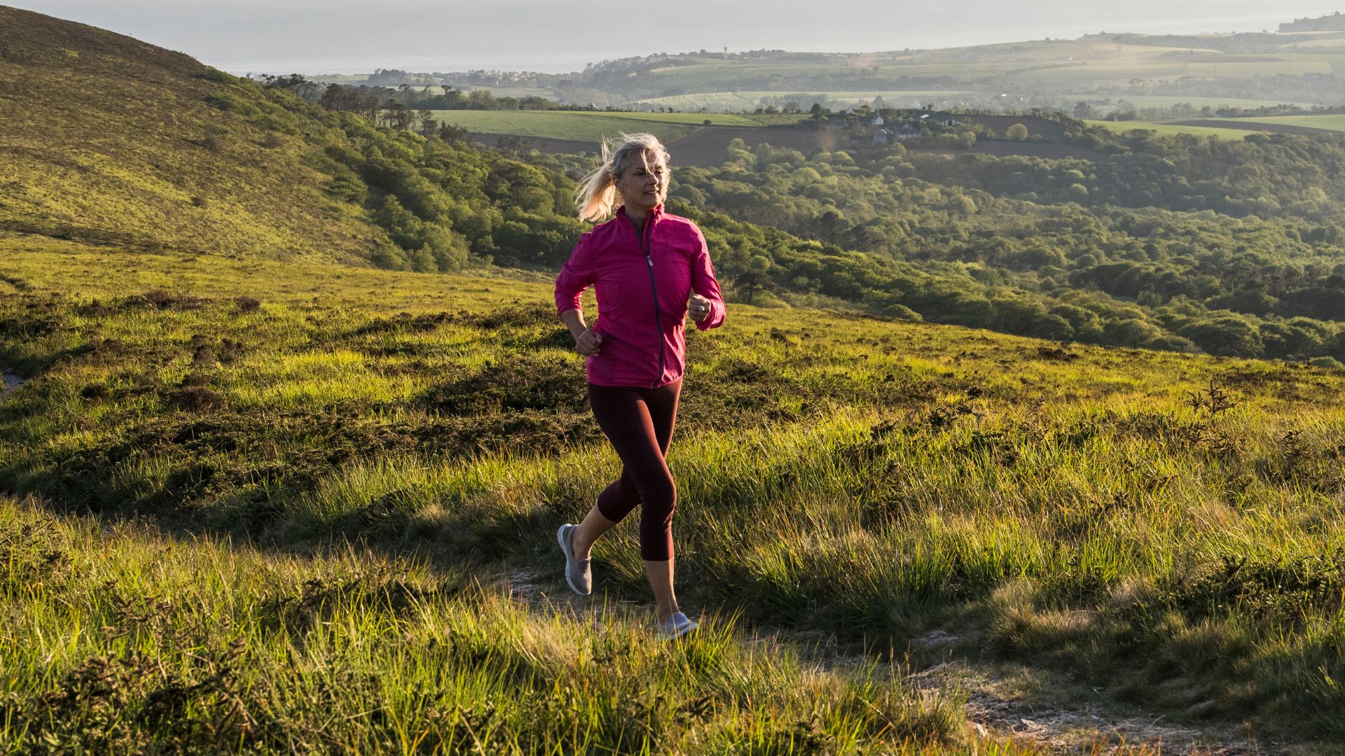Woman training for a marathon, running on hilltop in the countryside