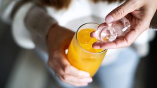 Woman's hands putting ice cubes into orange juice in a glass