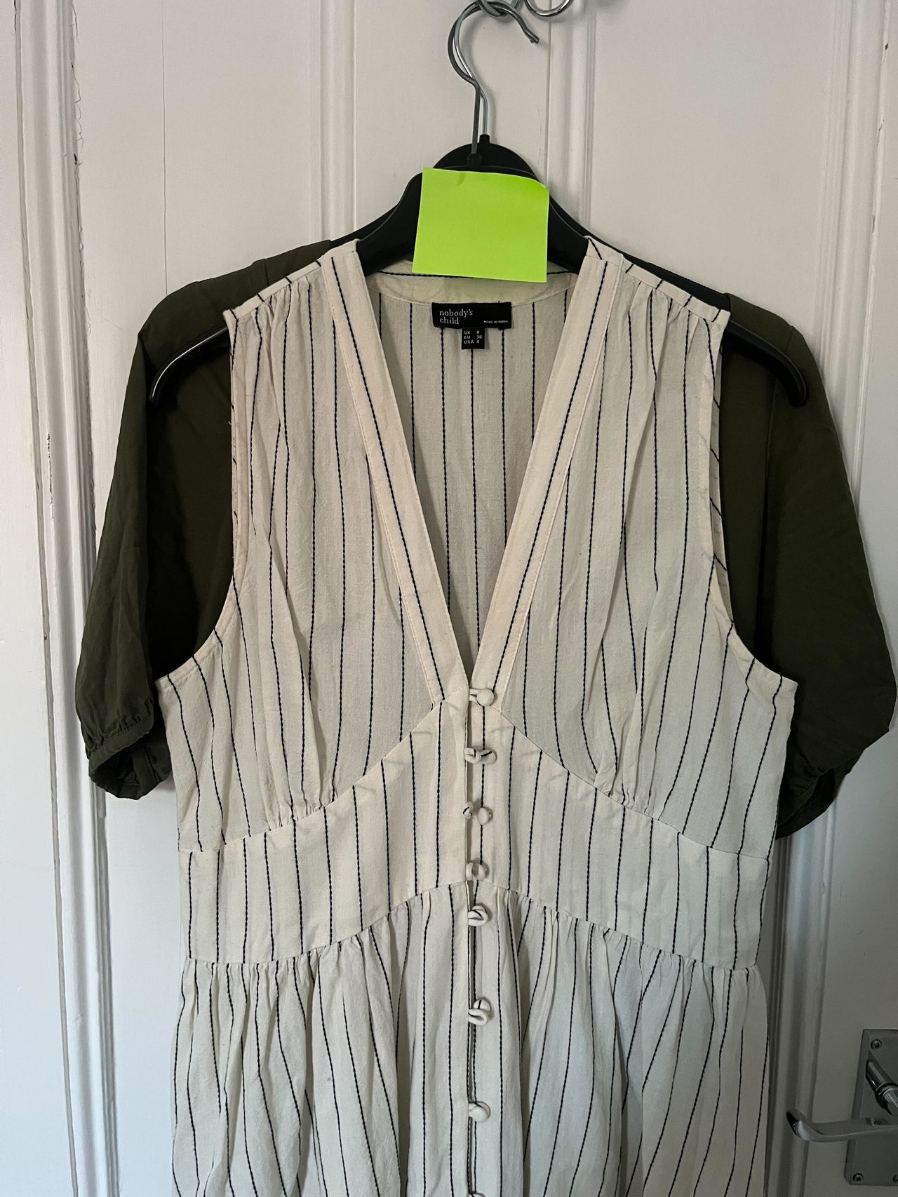 A cream stripped dress hanging on the back of a door with a green post it note on the hanger