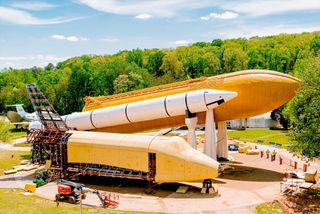 a big orange conical fuel tank mated with a white rocket sits horizontally with trees in the background