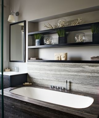 A bathroom with a large sink on a marble counter, and black shelves holding decorative objects