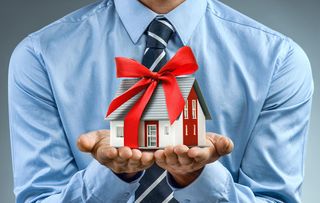 Worker in blue shirt holding house with red ribbon. Close up. Business concept