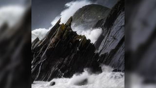 A landscape photograph of waves crashing against craggy rocks during a storm on the County Kerry coast in Ireland.