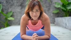 A woman smiles at the camera as she performs a plank exercise on a blue yoga mat.
