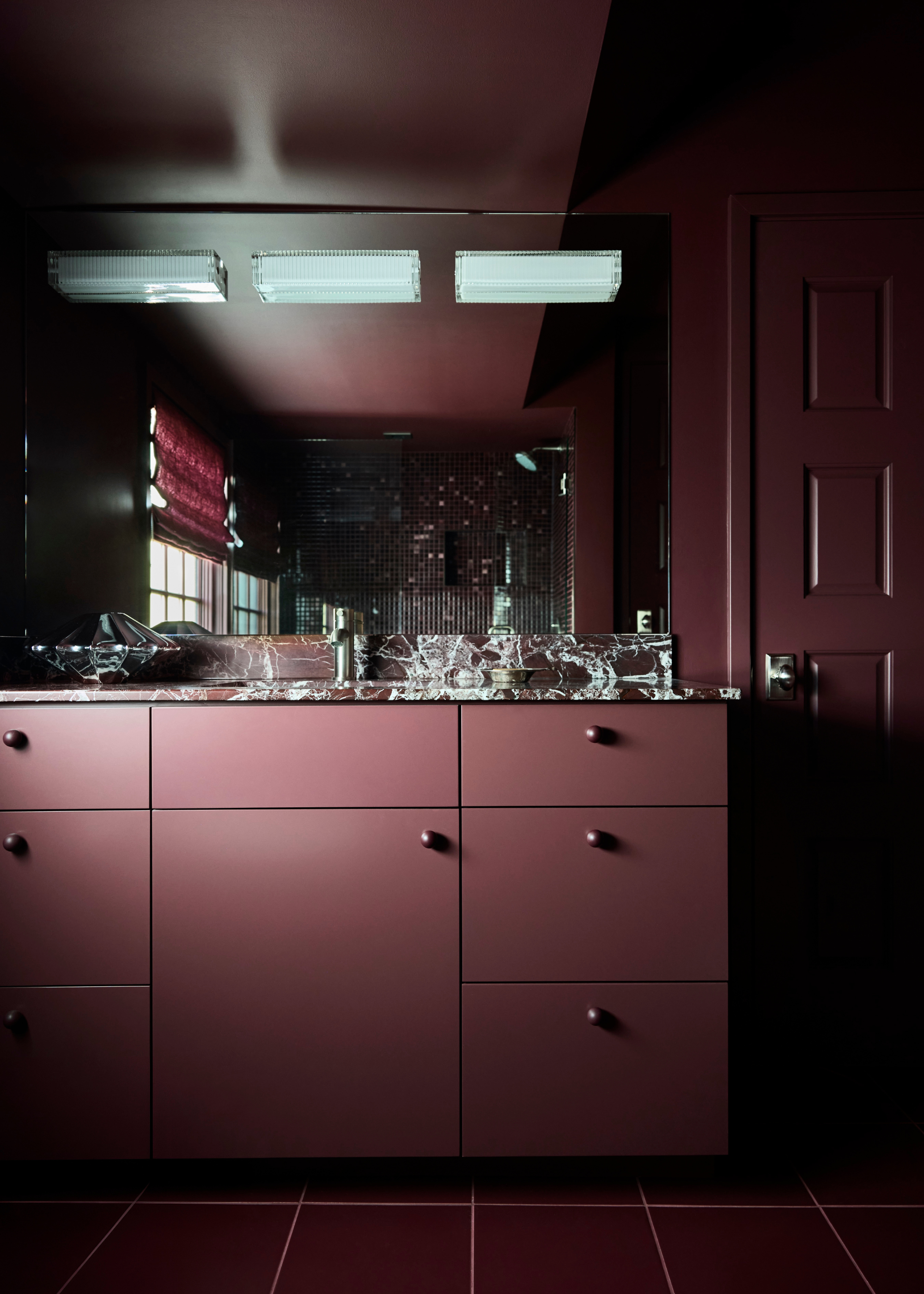 A dark burgundy colour-drenched bathroom pointing to the vanity which features a burgundy cabinet, and burgundy marble with chrome fetaures
