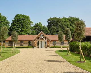 A large gravel driveway leading up to a wood-clad country home