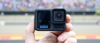 GoPro Hero 13 Black en una mano con una pista de carreras de fondo