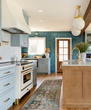 sky blue kitchen with teal tiled wall, white countertops, rug, hardwood floor, wood island, globe lights, brass fixtures and fittings