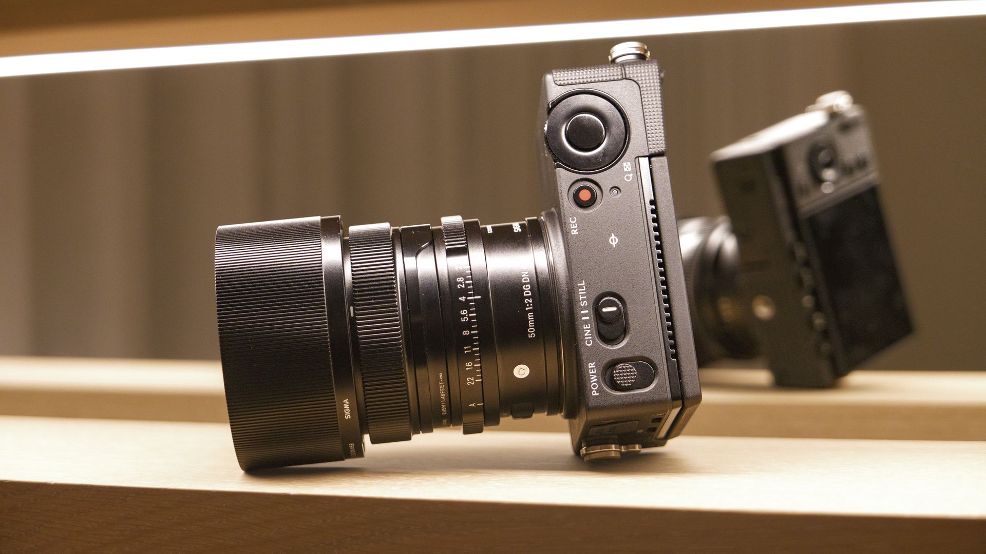 Sigma FP2 mirrorless camera with 50mm f/2 contemporary lenses attached, on a shelf, lit from above, view of its top plate