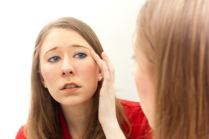 Young woman examining her face in the mirror