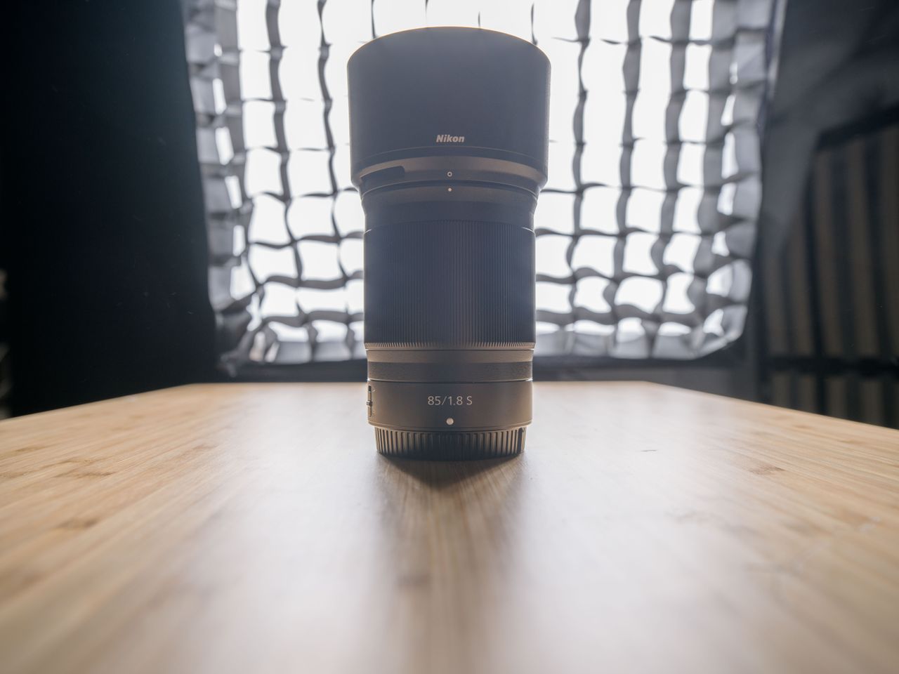 A backlit photo of a Nikon lens on a wooden surface with a studio light in the background. The shadow detail on the lens is now visible after post prodcution.