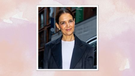 Image of Katie Holmes smiling with brunette ponytail and wearing a white T-shirt and satin navy blazer, on a pink watercolour background