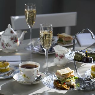 Teacup with tea, filled champagne glass, sandwiches on side plates on a lunch table