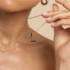 Woman holding 'L' initial necklace and wearing gold star earrings