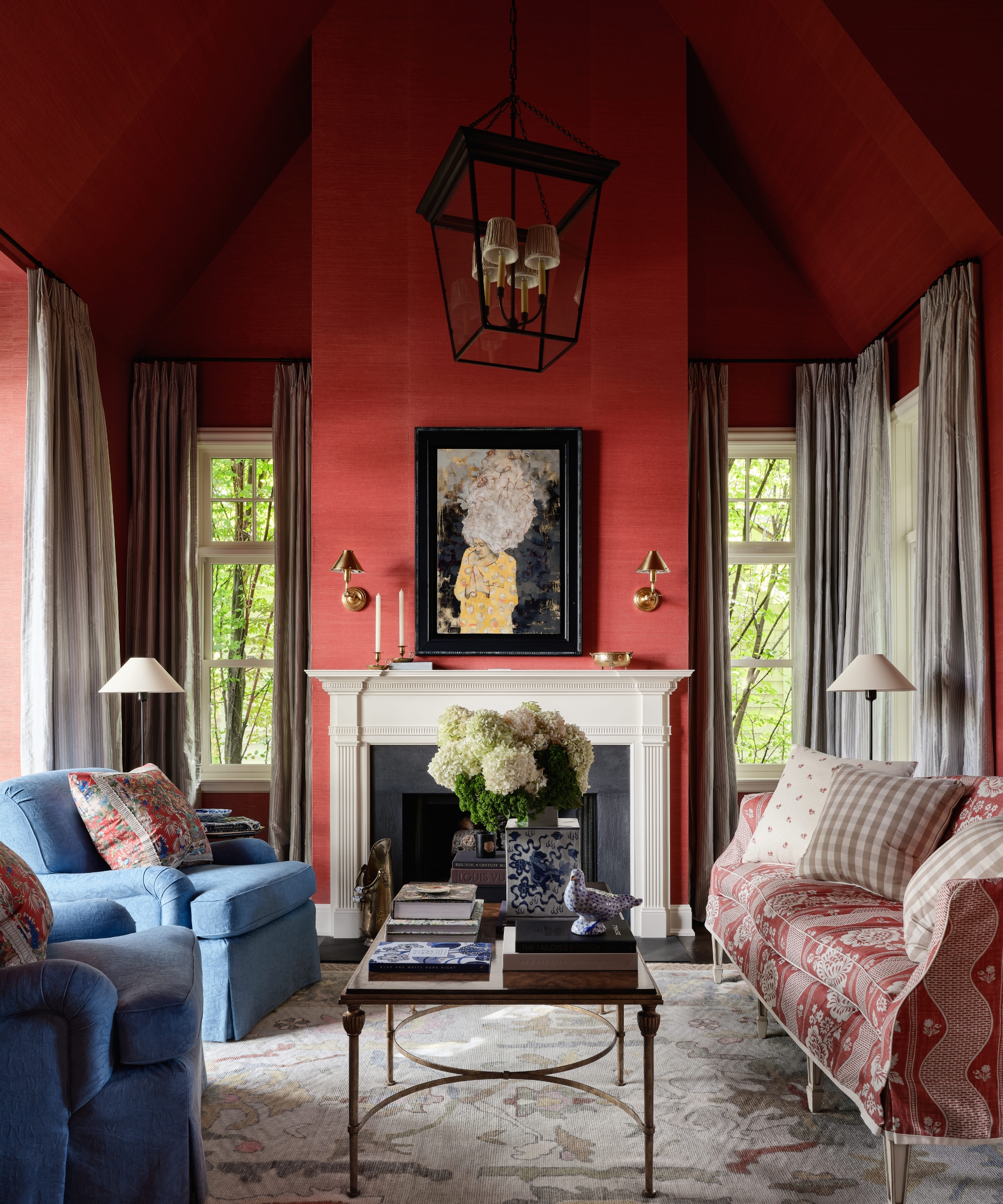 Red grasscloth living room with a white fireplace, blue armchairs, patterned settee, striped curtains and an oversized lantern.