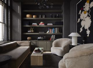 small living room drenched in dark gray with dark gray sofa, two fluffy armchairs, travertine coffee table and built-in display shelves