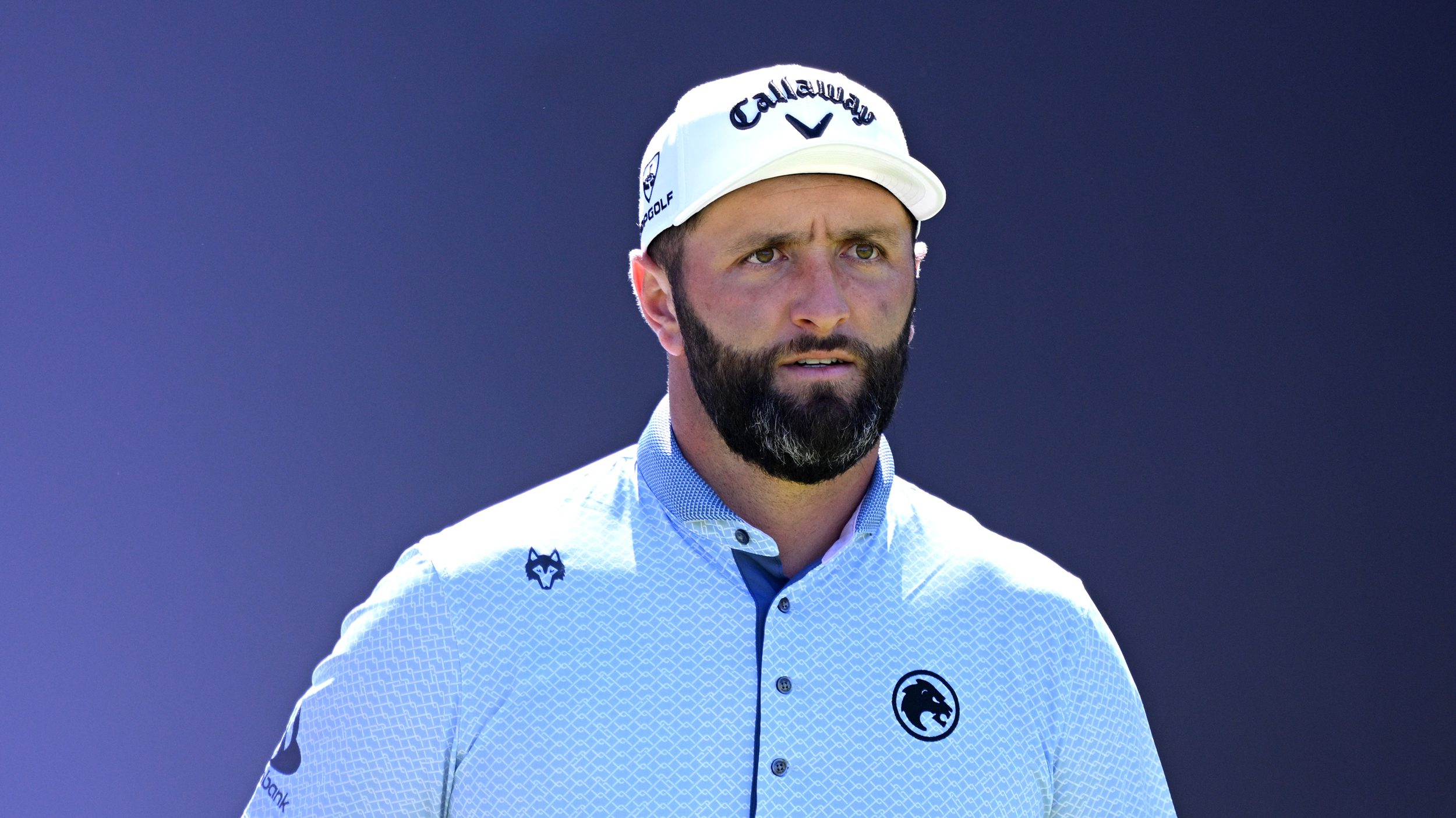 Jon Rahm from the chest up in front of a blue background