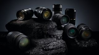 Eight assorted camera lenses arranged on a dark, textured rock surface with dramatic lighting