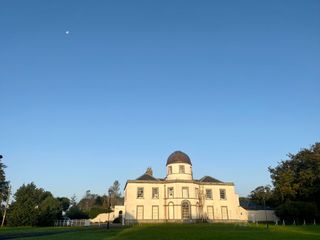 the moon is seen in the dusk sky above a building with a dome roof.