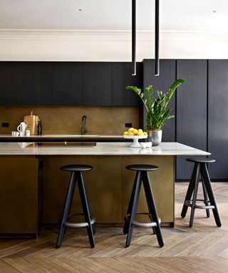 A black kitchen with brass backsplash and breakfast bar with black stools