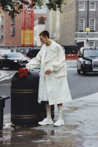 Man in Simone Rocha white jacket putting red roses in the bin on street