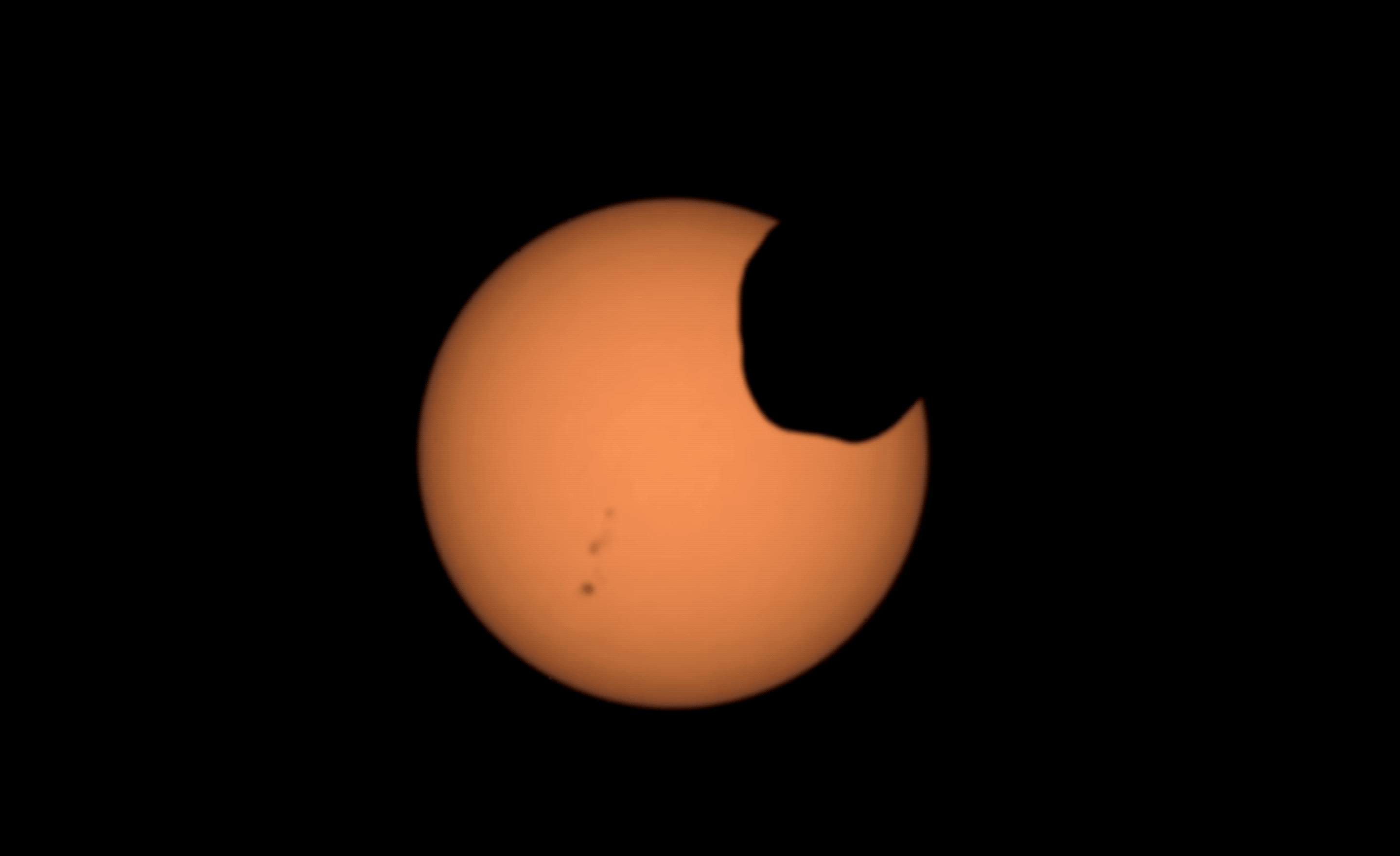 Mars' moon Phobos crosses the face of the sun, captured by NASA’s Perseverance rover with its Mastcam-Z camera. The faint black specks to the bottom left are sunspots.