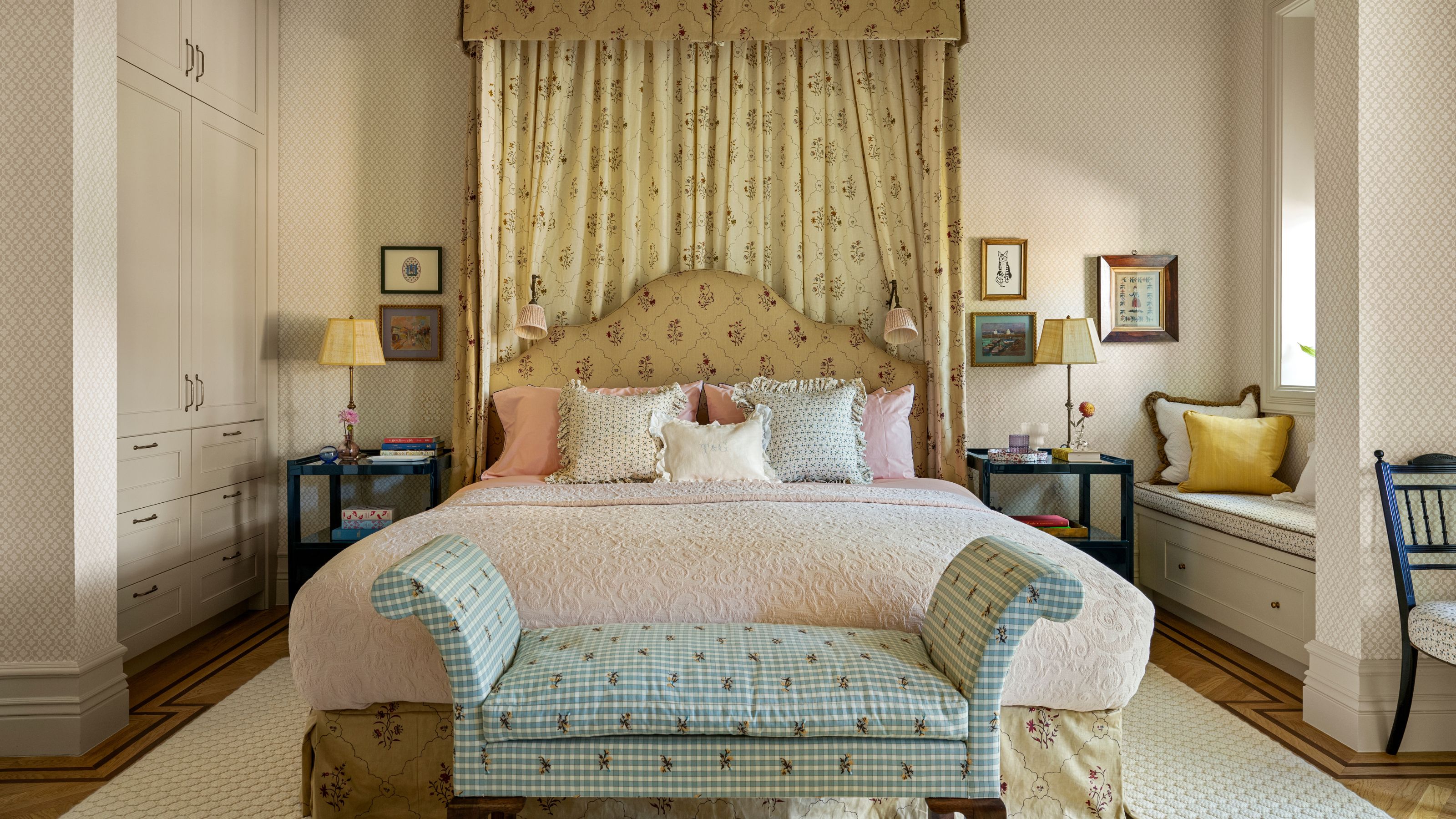 a grand master bedroom with a test canopy bed in floral print with a printed ottoman at the foot of the bed and custom cabinetry
