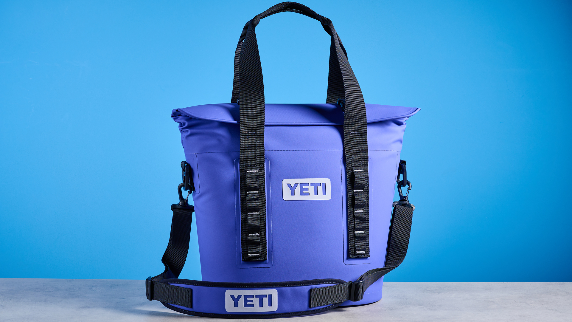 the yeti hopper m15 cool bag with a padded carry strap, handles, and a 15 quart capacity photographed with coke zero cans against a blue background