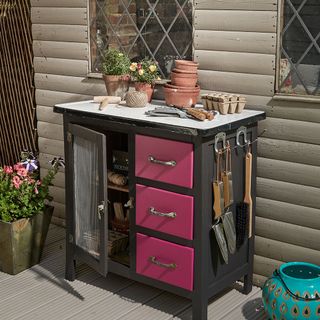 outdoor living area with wooden floor and black cabinet with pink drawers and gardening tools