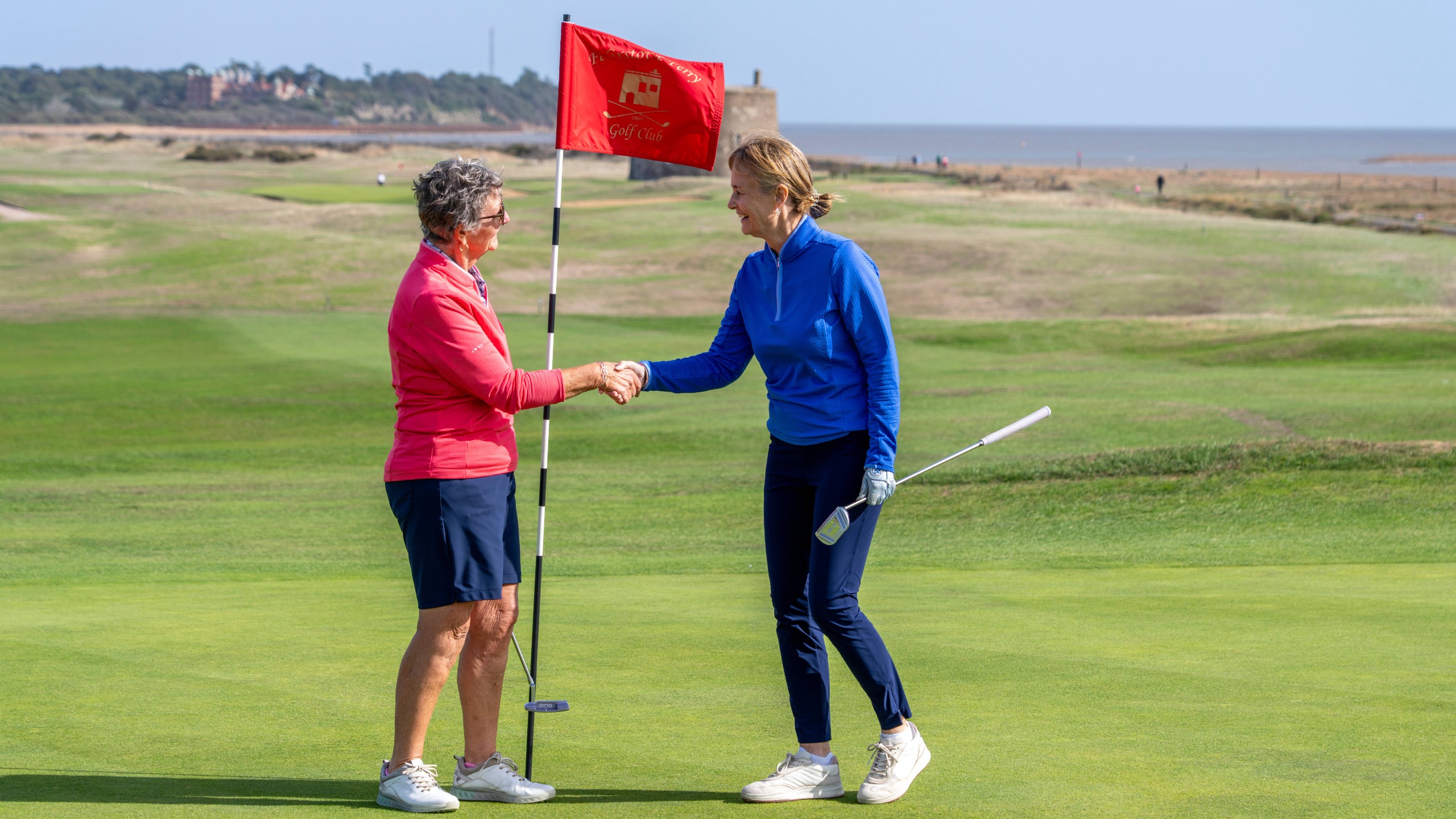 Gillian Anderson and Alison Root shaking hands on the 18th green at Felixstowe Ferry Golf Club