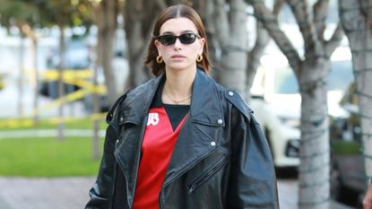 Hailey Bieber in a mini skirt, red jersey shirt, and oversized leather jacket