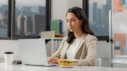 Woman eating sandwich at her desk.
