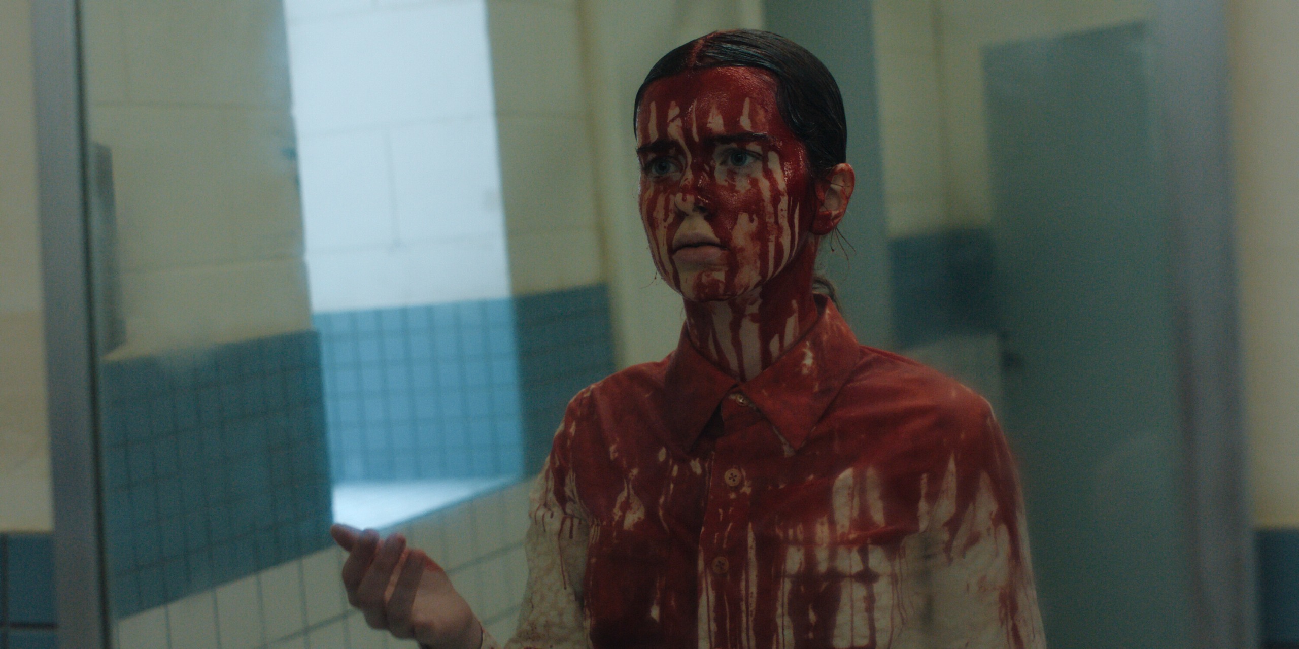 A teen girl covered in blood (Summer H. Howell as Carrie) looks at her reflection in a public bathroom mirror, in Prime Video's 'Carrie.'