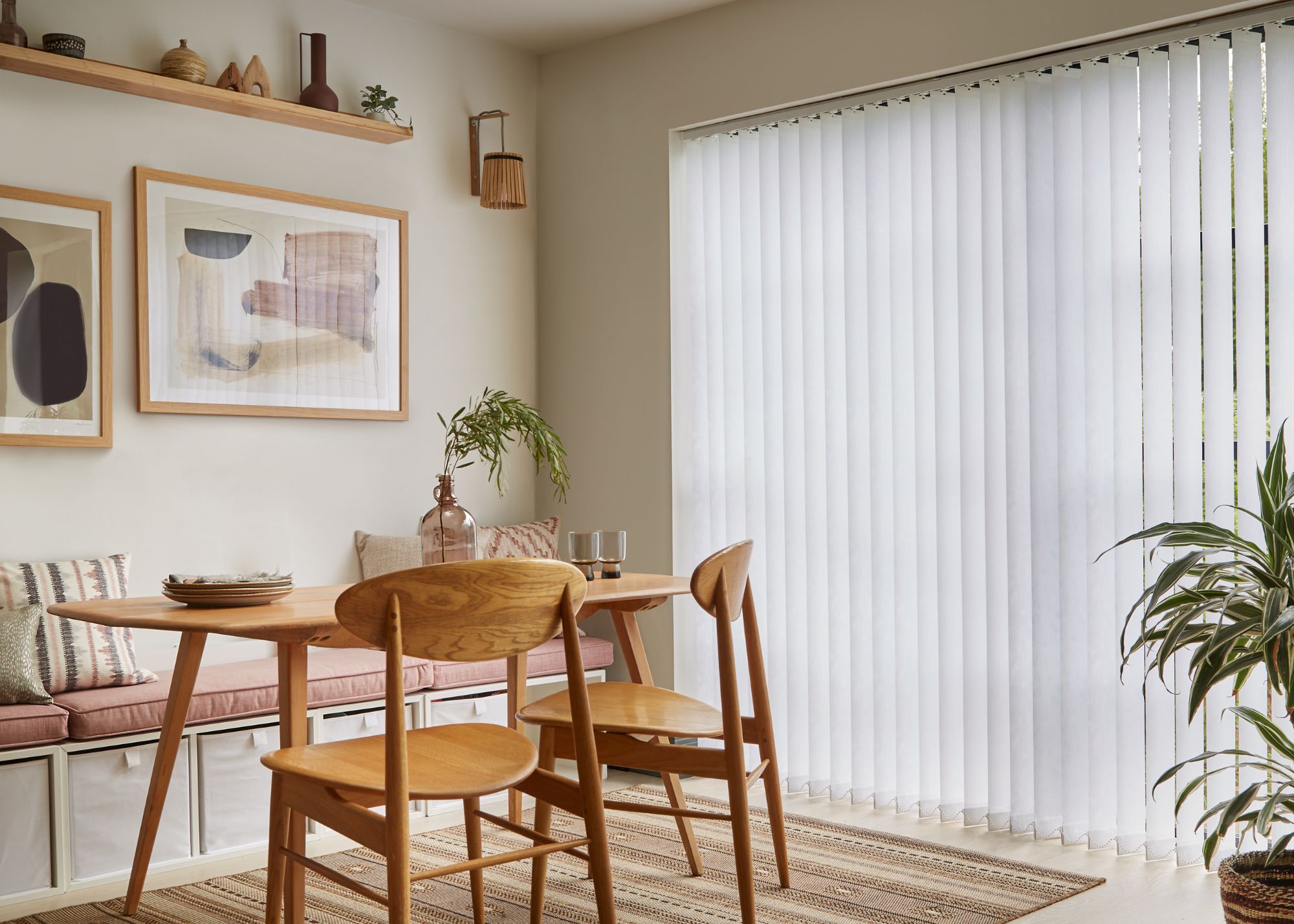 A neutral dining area with white vertical blinds on a sliding glass door, and a wooden dining table and chairs.