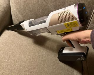 Vacuuming a grey upholstered couch using the handheld Shark Cordless Detect Pro Auto Empty System vac