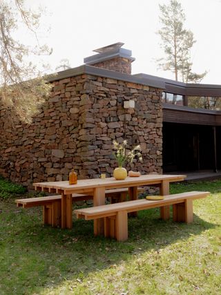 Pine outdoor long bench and table furniture set, set outside on grass beside a stone bricked building