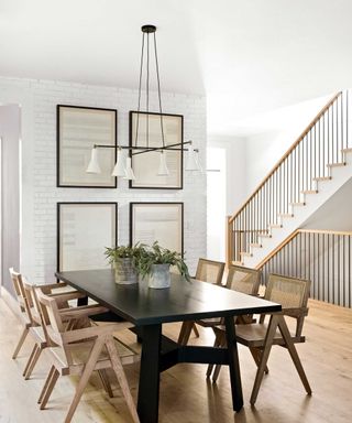 neutral dining room with dark wooden dining table and rattan chairs. the table is decorating with pot plants and a pendant light hangs overhead