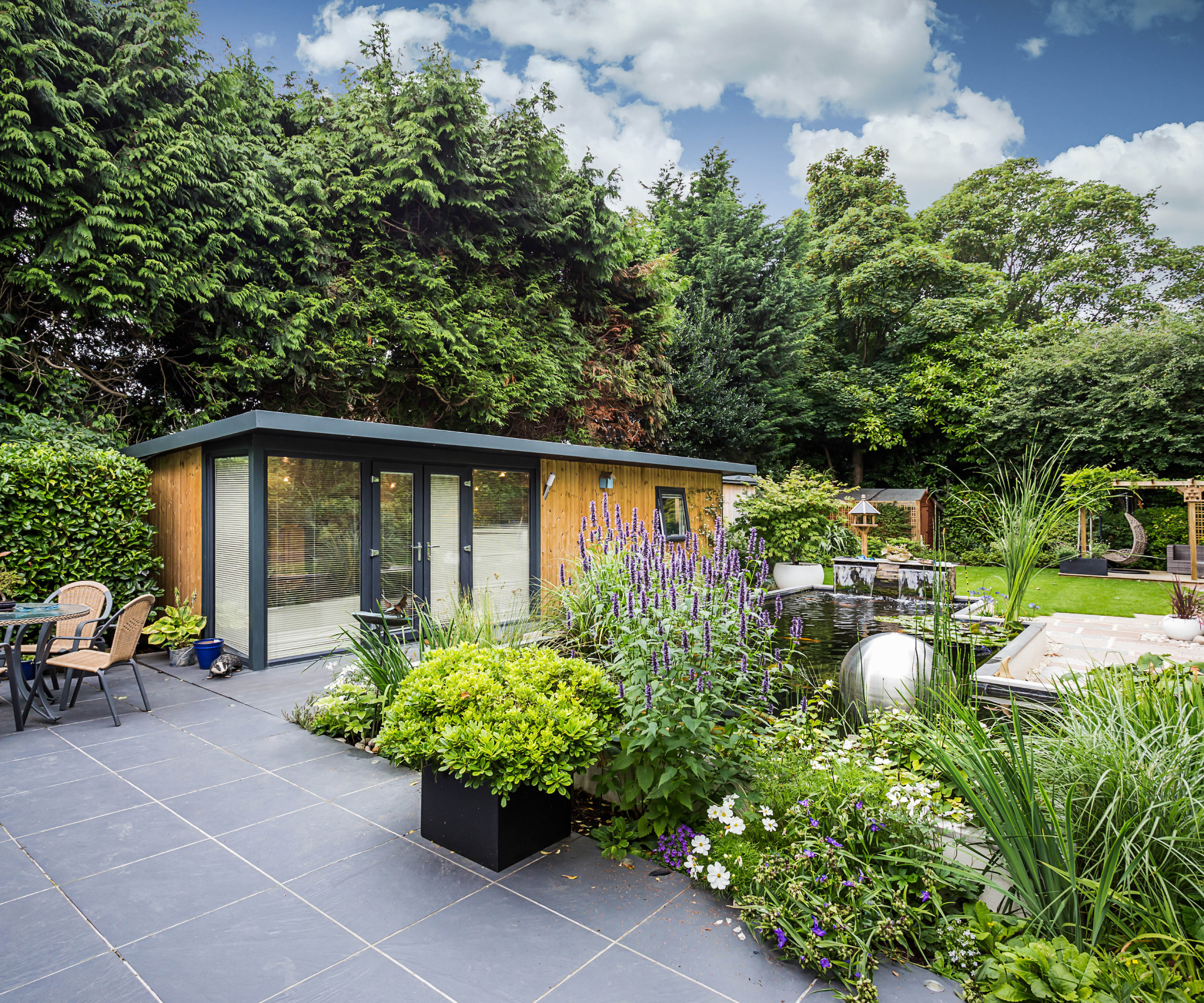 contemporary garden room with black patio, water feature, lush green planted areas