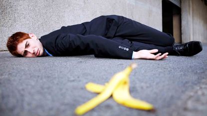 A businessman is on the ground after slipping on a banana peel.