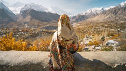 A woman sitting on wall and looking at Hunza valley in autumn