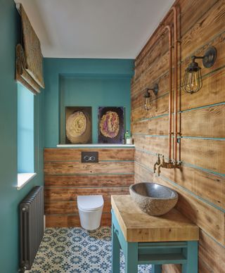 turquoise bathroom with wood cladding, exposed piping, vintage lighting, patterned floor tiles, blind at window