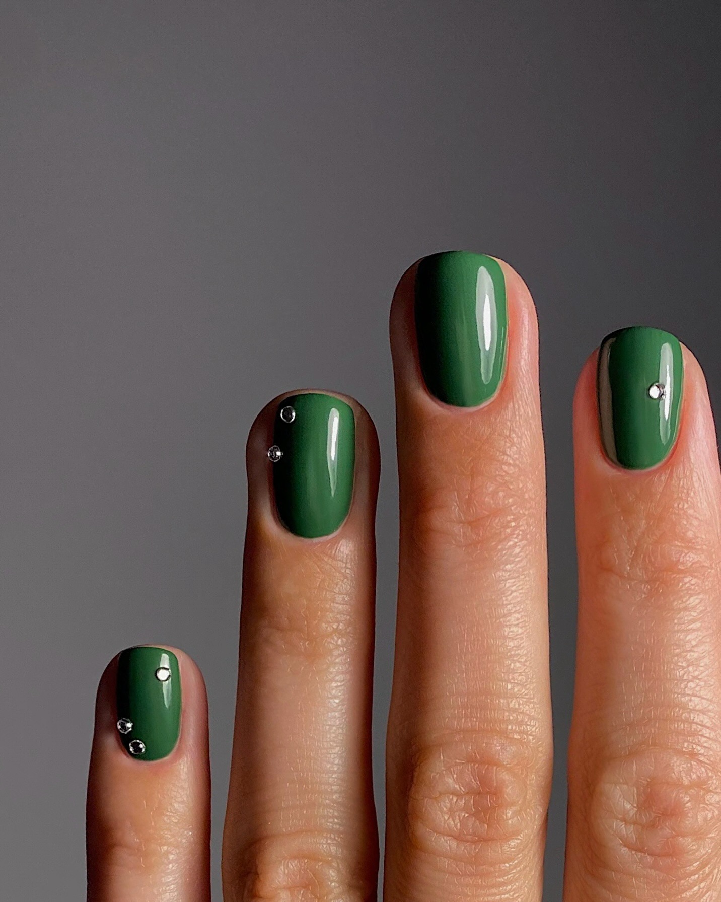 A short, forest green manicure with silver studs