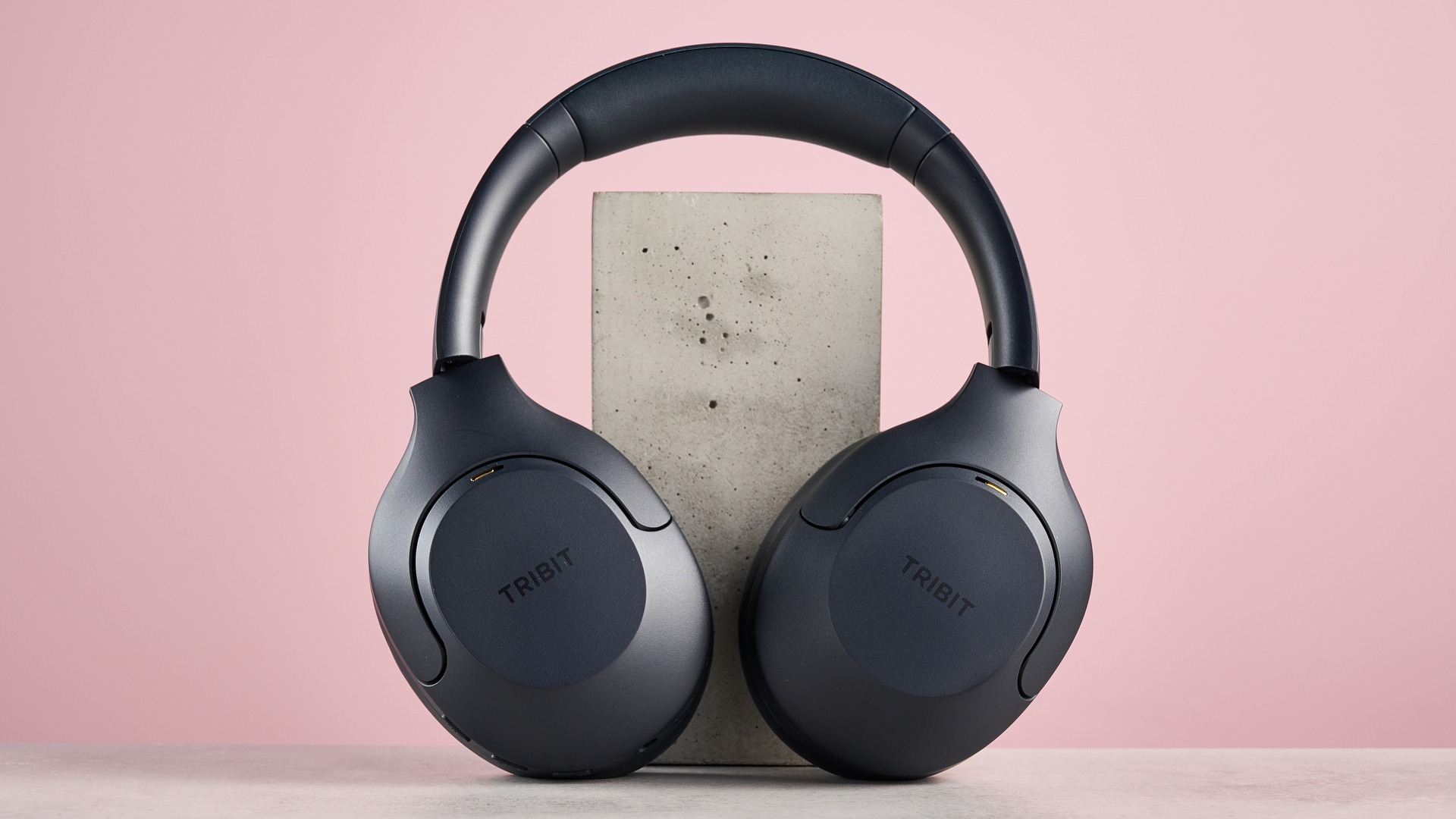 Tribit QuietPlus 81 leaning against block on pink background