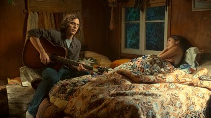 A still of a man playing the guitar and a woman laying in bed from TV show Daisy Jones and the Six