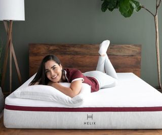 A woman lying on a Helix mattress against a gray wall.