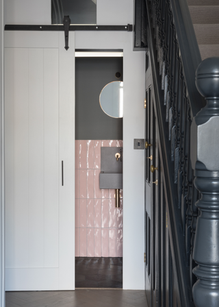 small pocket door toilet with pink tiles beneath a staircase