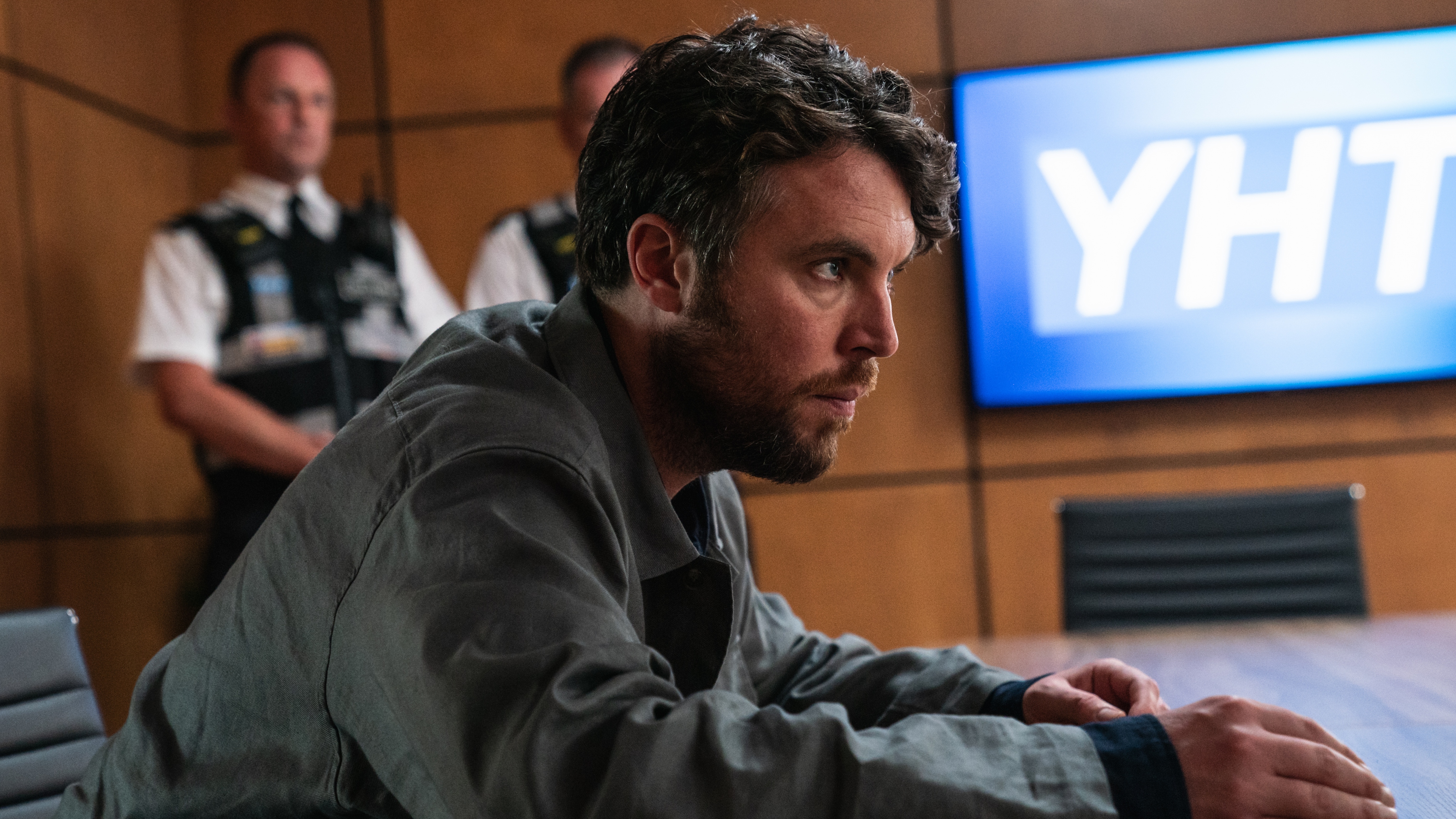 James looking stressed as he is questioned by the MIU in a wood panelled meeting room.