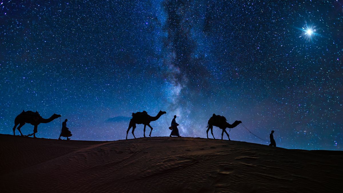 night sky scene with star of Bethlehem on the right and three wise men with their camels walking beneath. The milky way stretches through the night sky in the center of the image.